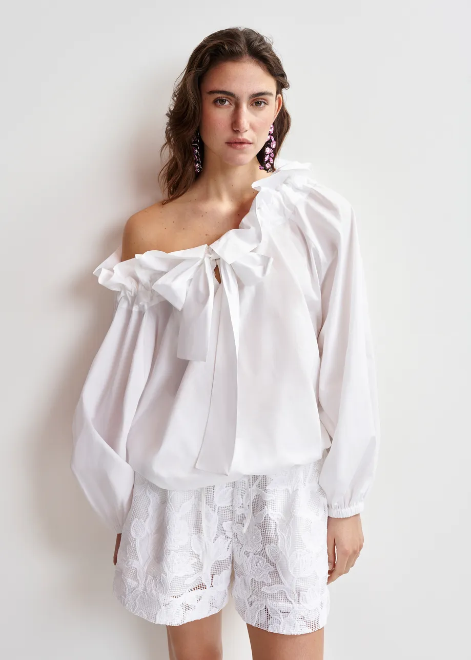 Top in cotone bianco con dettagli a volant, maniche voluminose e colletto con laccetti coordinati.