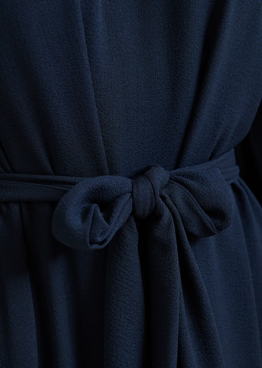 Donkerblauwe asymmetrische maxi-jurk met ruches aan de zoom en strikdetail bij de hals